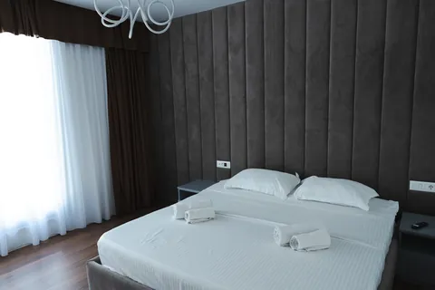 Double bedroom with a dark channel-tufted wall, white bedding and sheer curtains