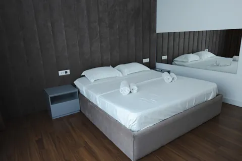 Double bed with fresh white linens and rolled towels beside a mirrored wall