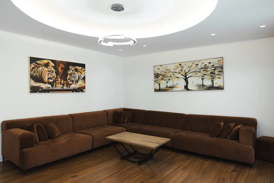 Living room with a brown velvet corner sofa, wooden coffee table and a softly lit circular ceiling