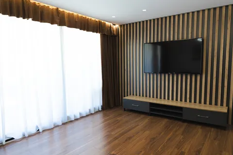 Lounge with a slatted wood feature wall, wall-mounted TV and wide curtained windows