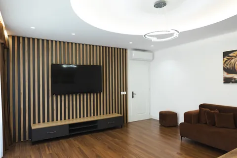 TV lounge with slatted wood wall and velvet sofa beneath a circular pendant light
