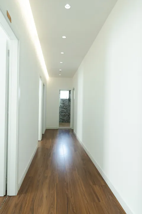 Long white hallway with warm wooden floors and cove lighting