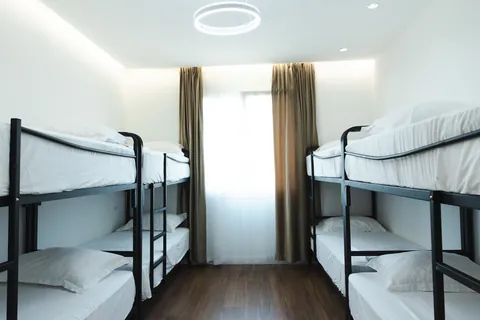 Room with two black metal bunk beds, white linens and a large curtained window