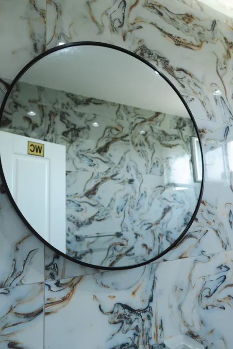 Bathroom with swirling marble-effect walls and a round black-framed mirror