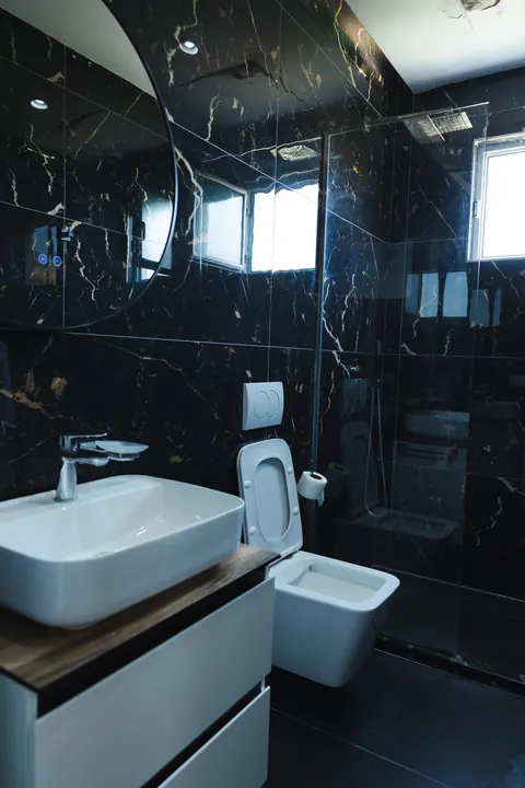 Black marble bathroom with a glass walk-in shower and modern basin