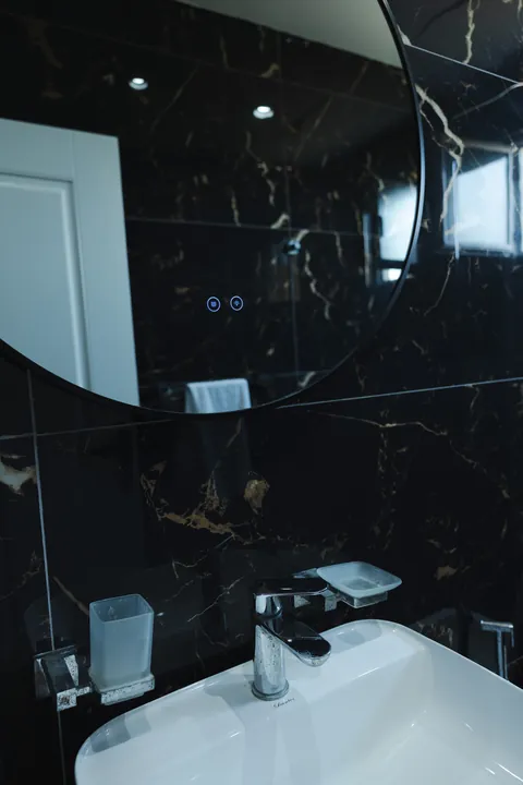 Black marble wall with a round mirror and a modern basin