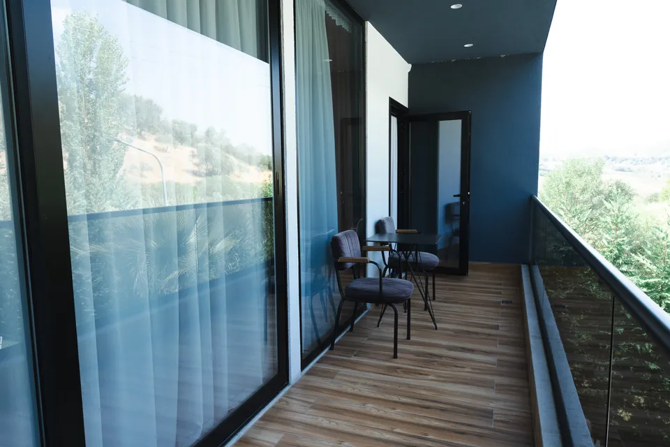 Long balcony with a glass railing, bistro seating and green hillside views